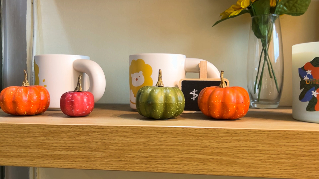 Sweetea café's display shelf decorated with colorful mini pumpkins and themed mugs, suggesting a cozy, festive atmosphere.