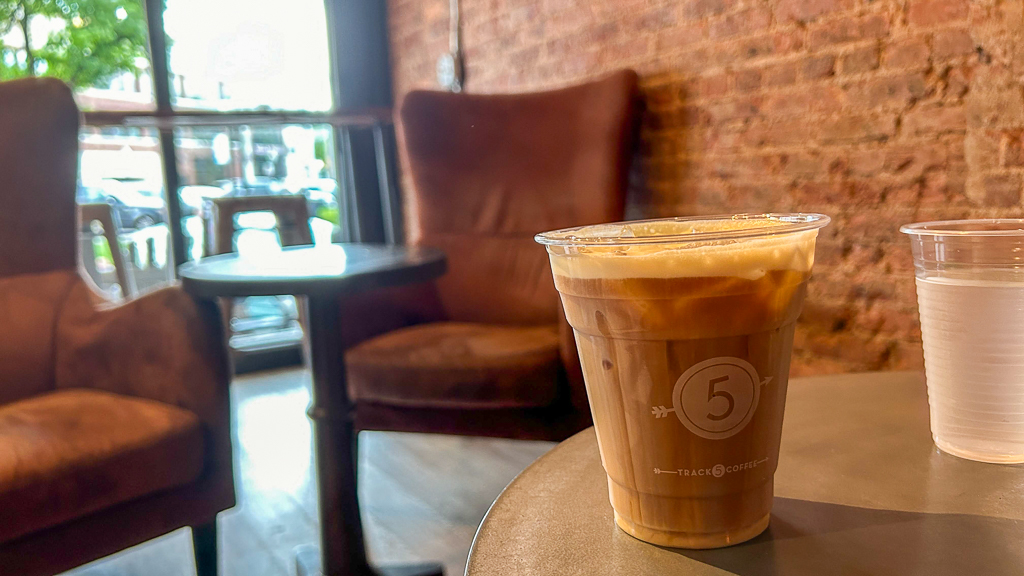 Casual setting inside Track 5 café with a wooden table and chair, featuring a cold coffee drink and a cup of water.